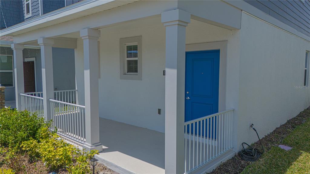 A covered porch features white columns, a white railing, and a bright blue front door — 1844 BRIGHT SKY DRIVE, KISSIMMEE, FL
