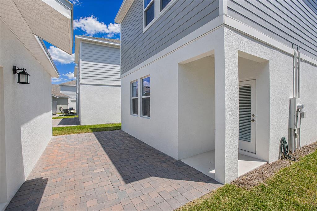 A paved patio sits between two houses with white stucco walls and gray siding — 1844 BRIGHT SKY DRIVE, KISSIMMEE, FL