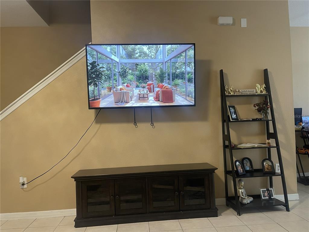 A wall-mounted television hangs above a dark wood media console next to a ladder shelf — 11517 DECLARATION DRIVE, TAMPA, FL