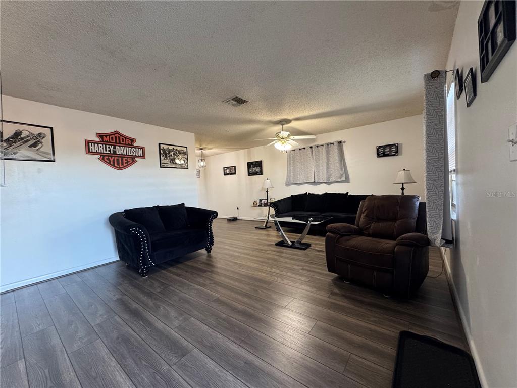 A living room features wood-look flooring, a ceiling fan, and black and brown furniture — 147 EVERGREEN DRIVE, LAKE WALES, FL