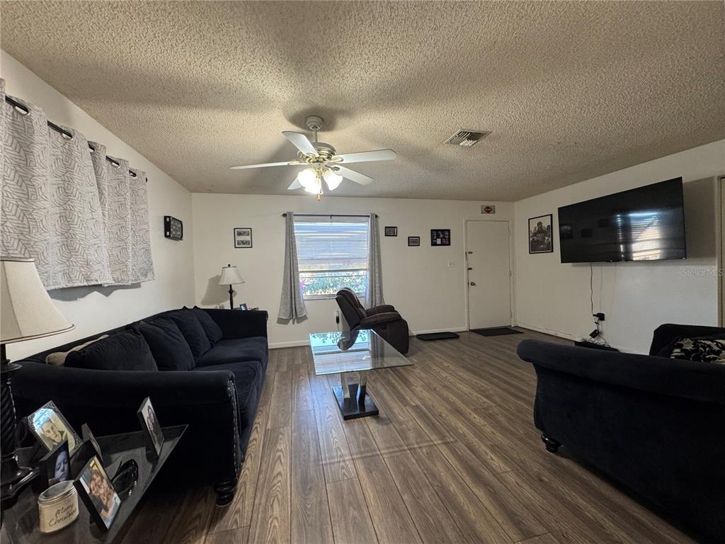 A living room features dark sofas, a glass coffee table, and wood-look flooring — 147 EVERGREEN DRIVE, LAKE WALES, FL