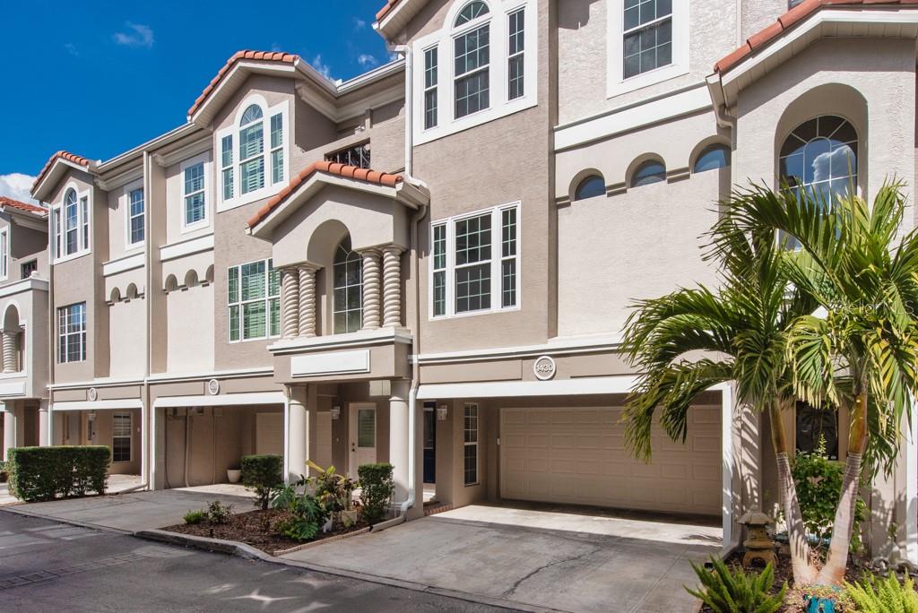 A multi-story townhouse exterior with a beige stucco facade, arched windows, and ground-level garages — 1430 MANATEE CIRCLE, TARPON SPRINGS, FL