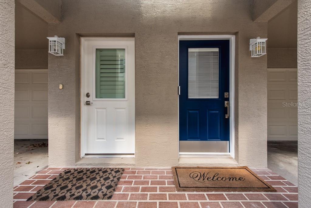 Two exterior doors, one white and one blue, sit side-by-side on a brick porch — 1430 MANATEE CIRCLE, TARPON SPRINGS, FL