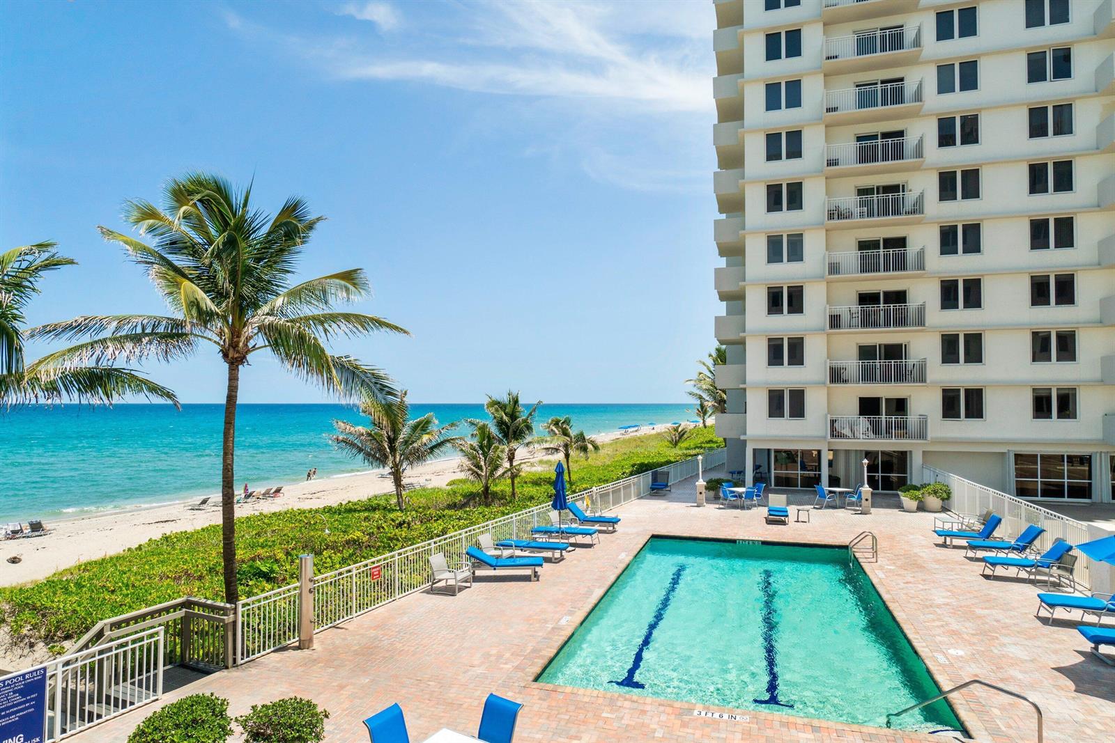 An outdoor swimming pool sits on a patio next to a multi-story building and beach — 3215 S Ocean Boulevard # 407, Highland Beach FL 33487, HIGHLAND BEACH, FL