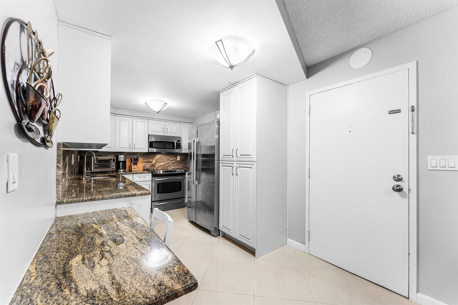 A kitchen features white cabinets, granite countertops, stainless steel appliances, and a tile floor — 3215 S Ocean Boulevard # 407, Highland Beach FL 33487, HIGHLAND BEACH, FL