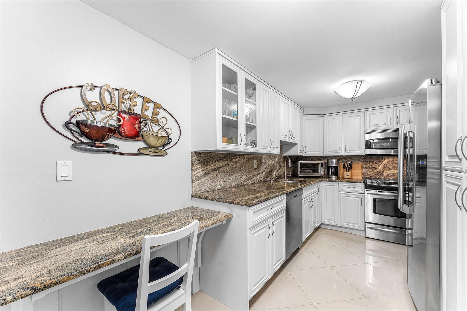 A kitchen with white cabinets, granite countertops, stainless steel appliances, and a small breakfast bar — 3215 S Ocean Boulevard # 407, Highland Beach FL 33487, HIGHLAND BEACH, FL