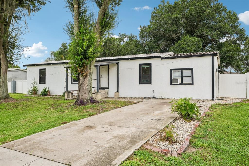 A single-story white house with a black-trimmed roof and a concrete driveway — 8620 INDIAN RIDGE TRAIL, LAKELAND, FL