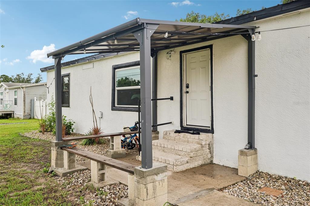 The exterior of a white house features a metal patio cover over a concrete porch — 8620 INDIAN RIDGE TRAIL, LAKELAND, FL