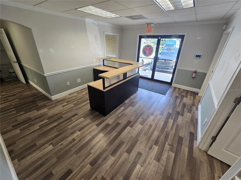 An office reception area features a dark wood-look floor, a reception desk, and glass doors — 7434 S FEDERAL HWY 1 HIGHWAY, PORT ST LUCIE, FL