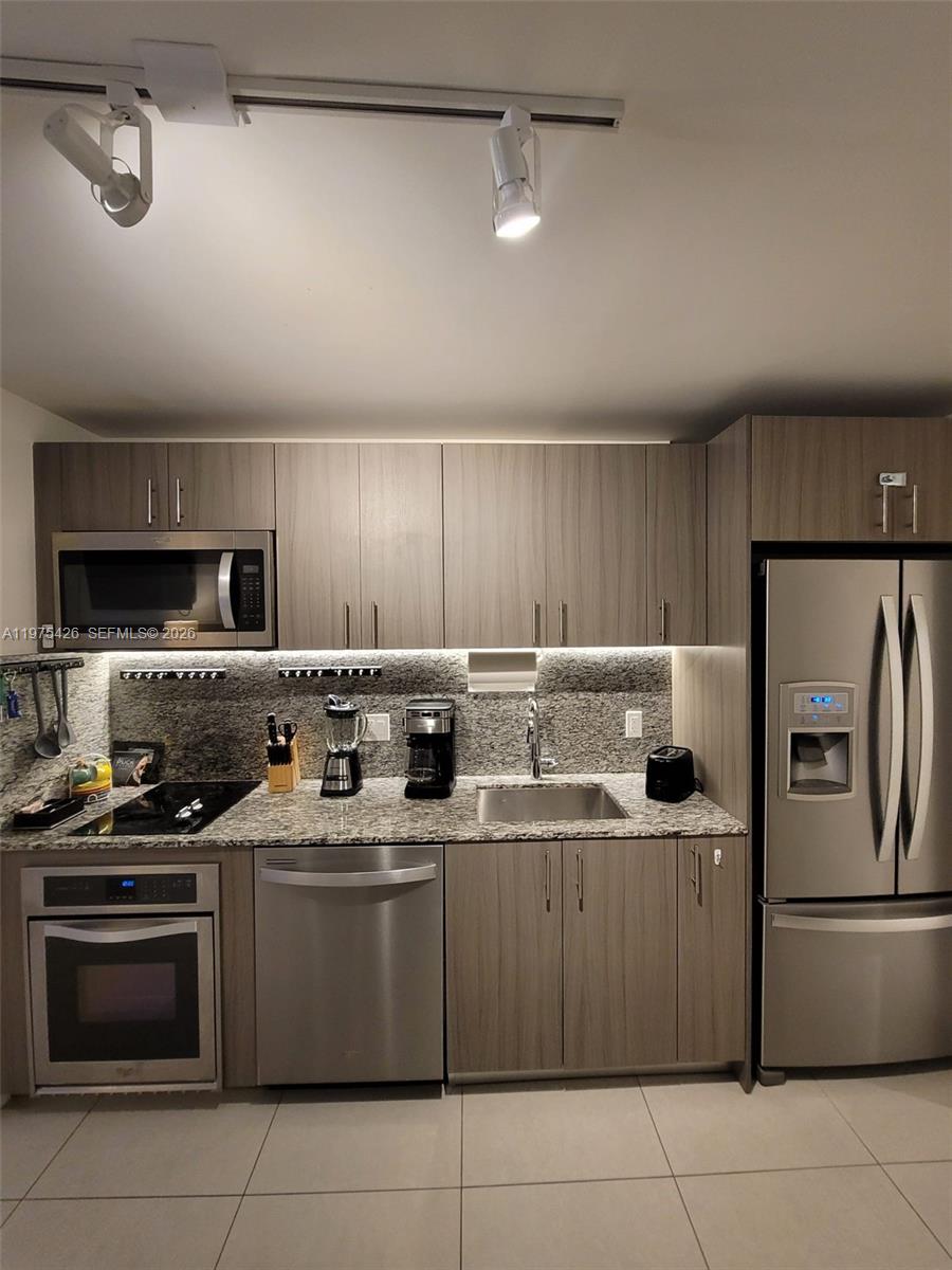 A modern kitchen features wood-grain cabinets, stainless steel appliances, and granite countertops — 5350 NW 84th Ave # 1116, Doral FL 33166, DORAL, FL