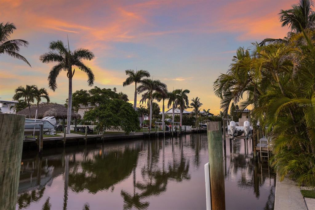 A canal view at sunset features palm trees, boat docks, and moored motorboats — 212 OAK AVENUE, ANNA MARIA, FL