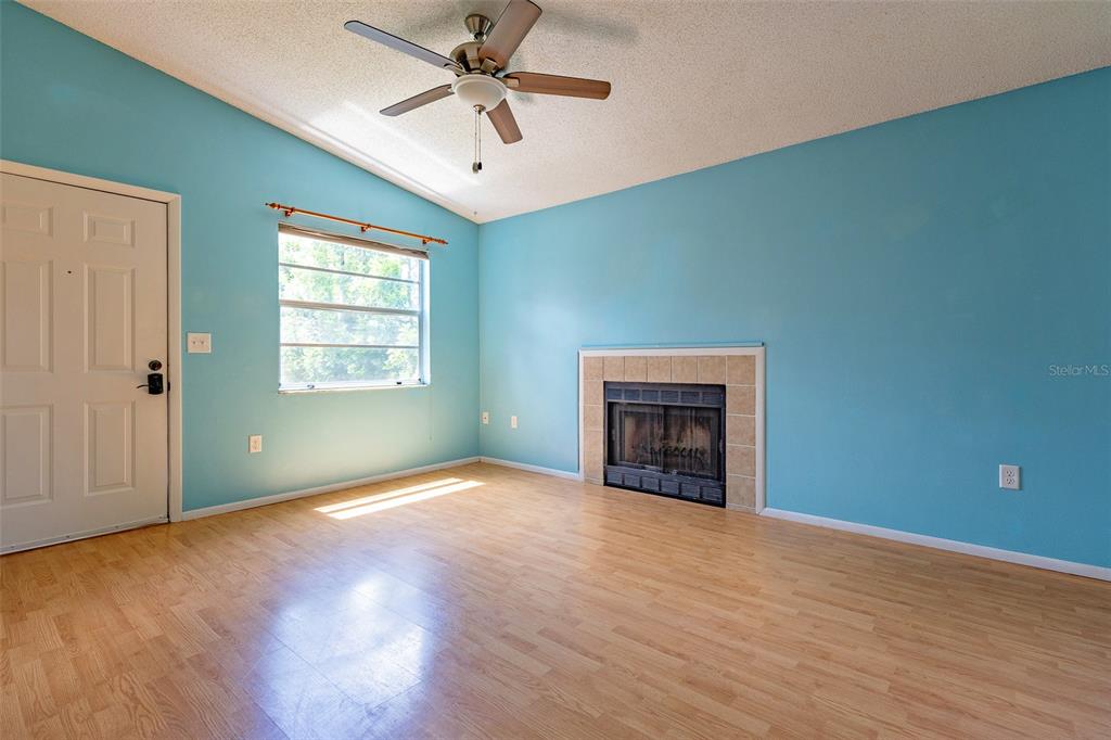 A living room features light blue walls, wood-look flooring, a ceiling fan, and a fireplace — 3774 59TH AVENUE W UNIT 3774, BRADENTON, FL