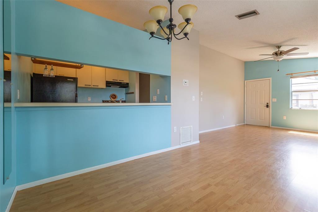 A living room with light wood flooring, blue accent walls, and an open kitchen pass-through — 3774 59TH AVENUE W UNIT 3774, BRADENTON, FL