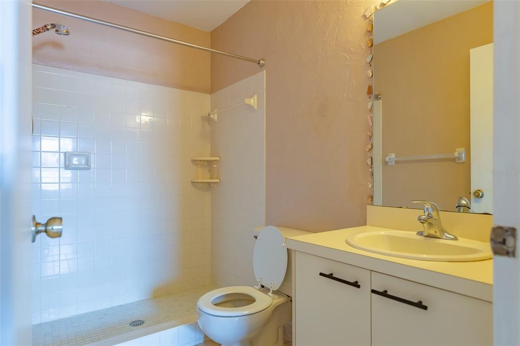 A bathroom features a white vanity, a toilet, and a tiled shower with a curtain rod — 3774 59TH AVENUE W UNIT 3774, BRADENTON, FL