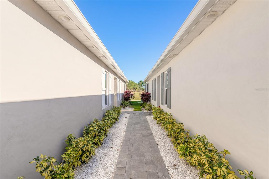 A paved walkway leads between two exterior house walls lined with white gravel and shrubs — 3088 ISLES WAY, NEW SMYRNA BEACH, FL