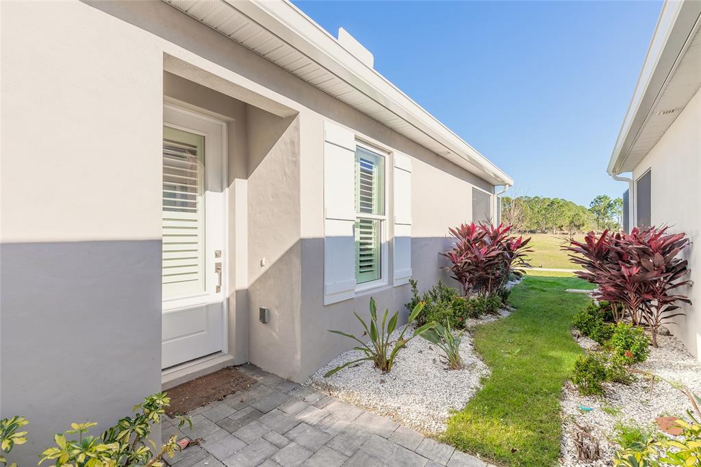 A side view of a house exterior featuring a white door, window shutters, and landscaping — 3088 ISLES WAY, NEW SMYRNA BEACH, FL