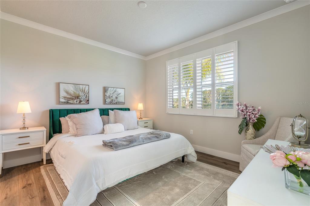 A bedroom features a green velvet headboard, white bedding, plantation shutters, and a patterned rug — 3088 ISLES WAY, NEW SMYRNA BEACH, FL