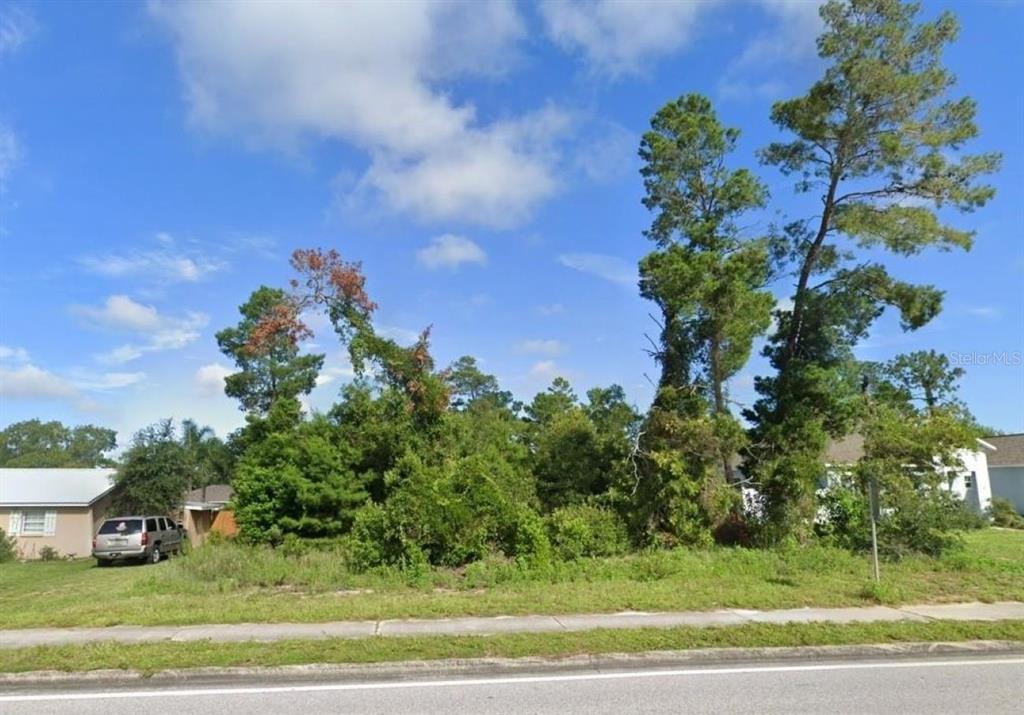 A vacant, tree-covered lot sits between two residential houses under a blue sky — 6241 MARINER BOULEVARD Lot 31, SPRING HILL, FL