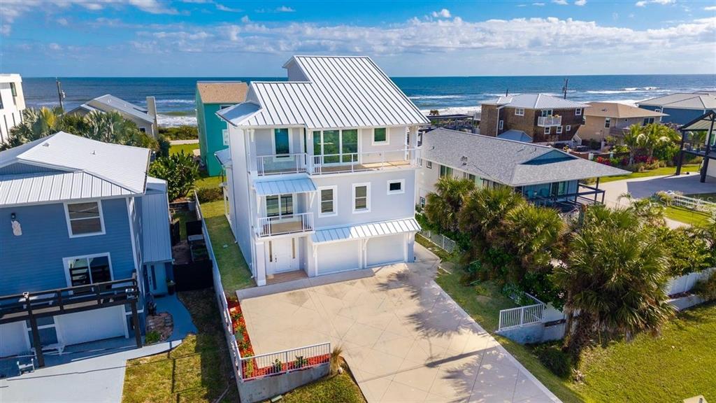 An elevated three-story coastal house with a metal roof and a concrete driveway — 6191 TURTLEMOUND ROAD, NEW SMYRNA BEACH, FL