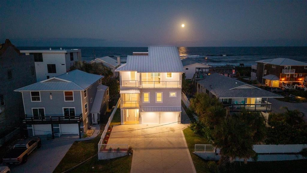An aerial view of a three-story beach house at night with a full moon overhead — 6191 TURTLEMOUND ROAD, NEW SMYRNA BEACH, FL