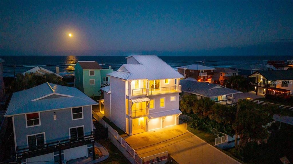 An aerial view of a multi-story coastal house at night with a full moon overhead — 6191 TURTLEMOUND ROAD, NEW SMYRNA BEACH, FL