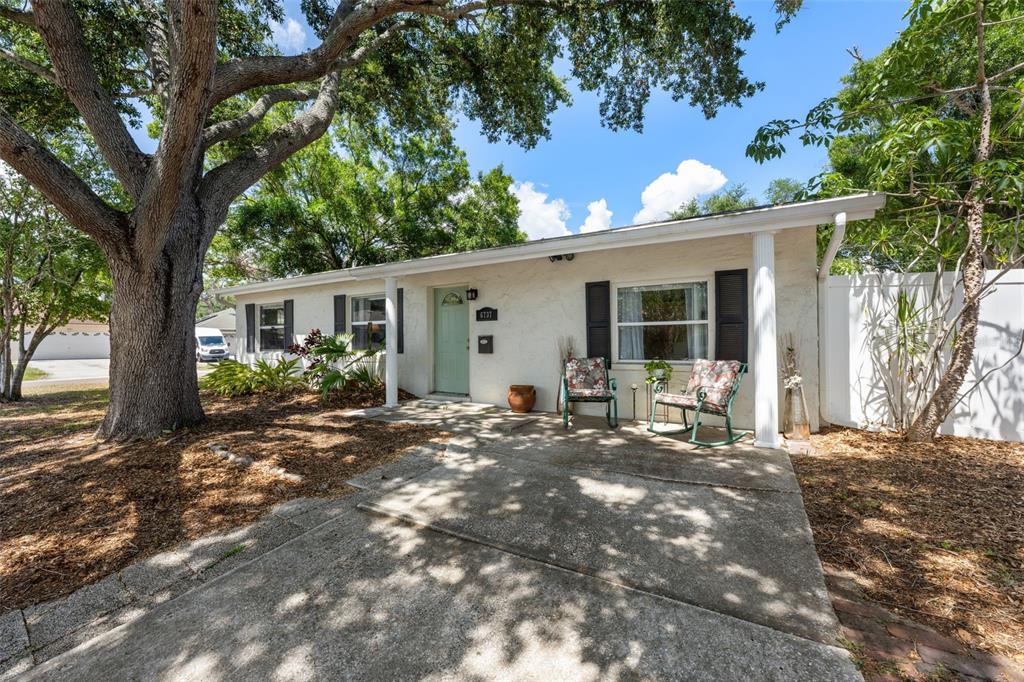 A single-story white house with a front porch, rocking chairs, and a large oak tree — 6737 LAUREL STREET N, ST PETERSBURG, FL