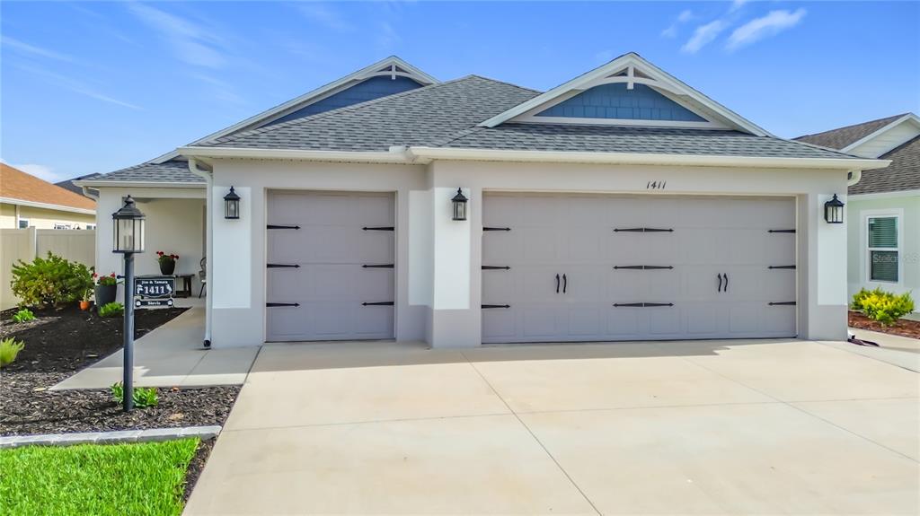 A single-story house features a three-car garage, light-colored stucco walls, and a gabled roof — 1411 FRANKLIN COURT, THE VILLAGES, FL