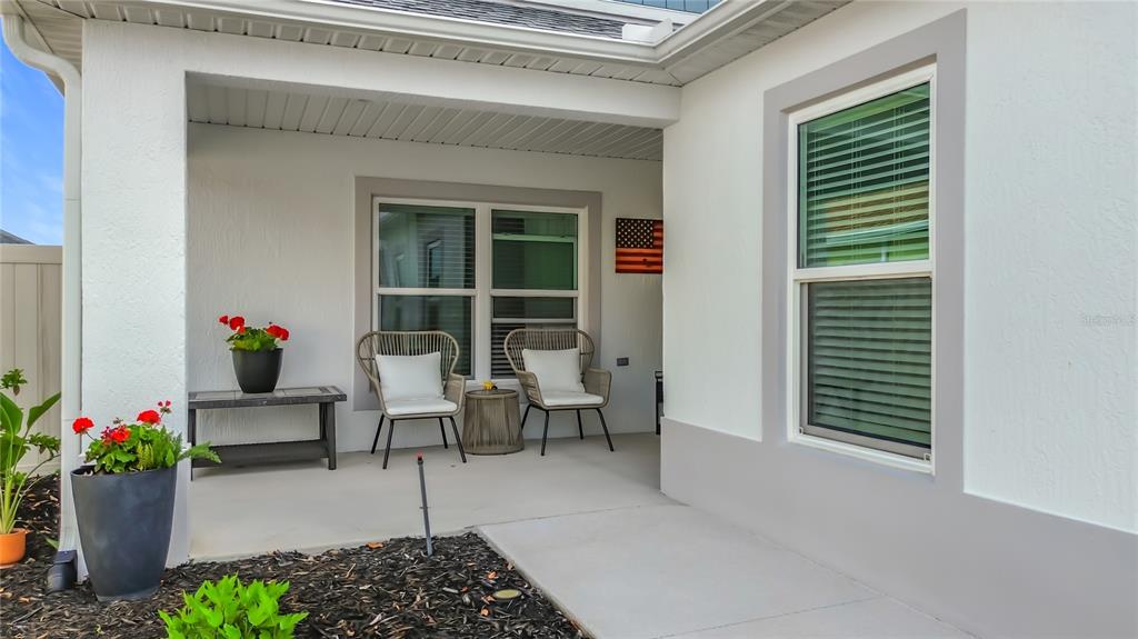 A covered patio features two wicker chairs, a small table, and potted plants — 1411 FRANKLIN COURT, THE VILLAGES, FL