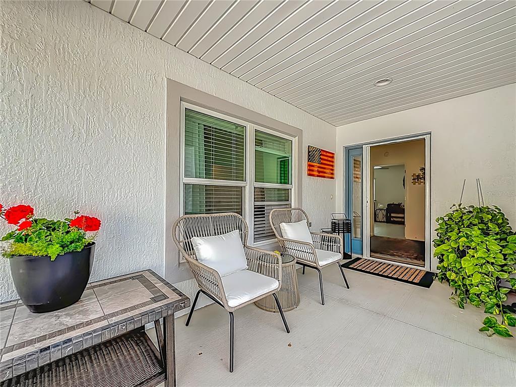 A covered patio features two wicker chairs, a side table, potted plants, and an entryway — 1411 FRANKLIN COURT, THE VILLAGES, FL