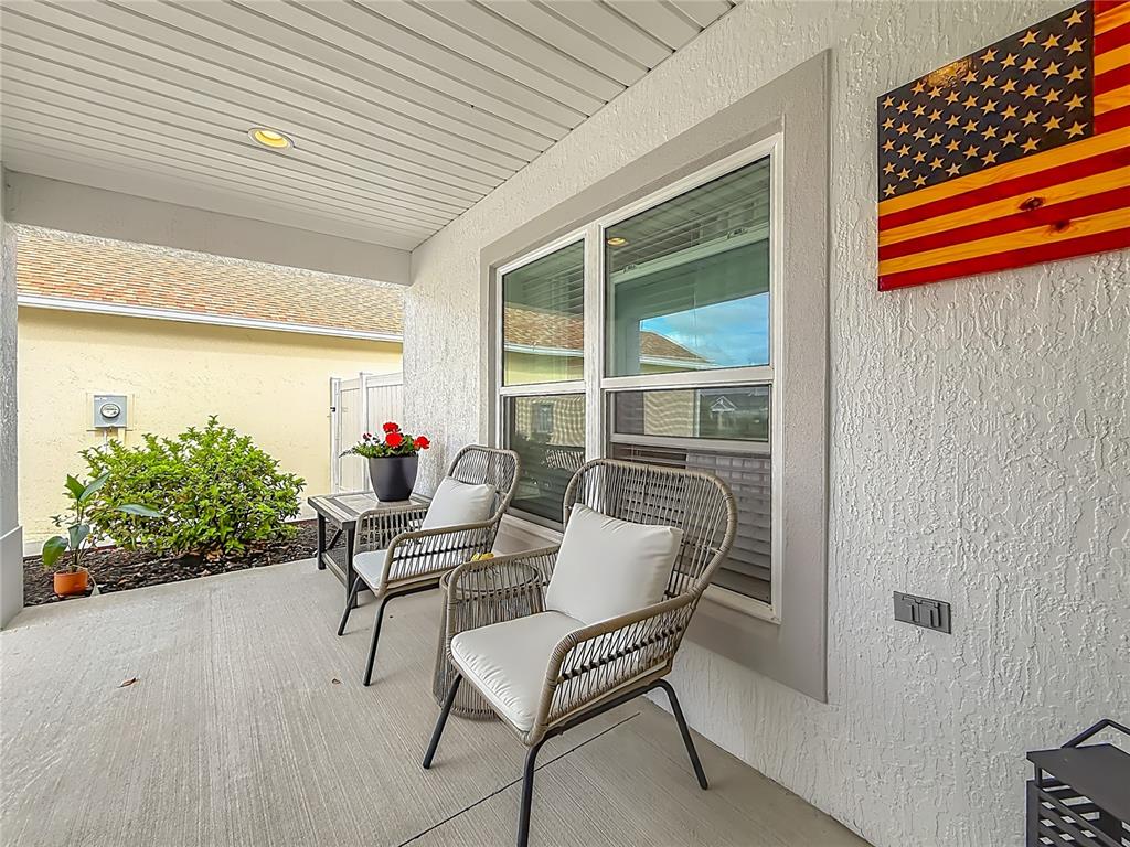A covered patio features two wicker chairs, a small table, and a wooden American flag — 1411 FRANKLIN COURT, THE VILLAGES, FL