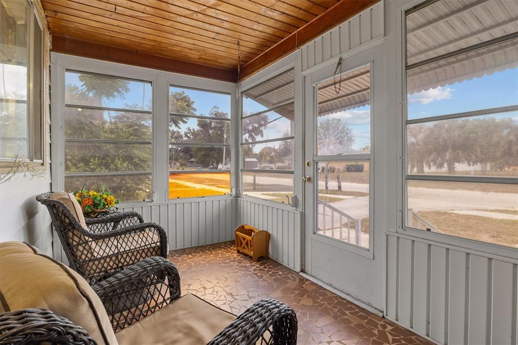 A screened-in porch features a wood-paneled ceiling, tiled floor, wicker furniture, and large windows — 207 S PERRY AVENUE, FORT MEADE, FL