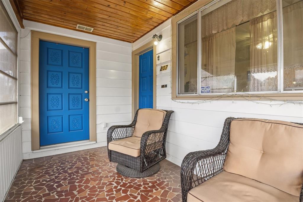 A covered porch features a blue door, two wicker chairs, and a tiled floor — 207 S PERRY AVENUE, FORT MEADE, FL