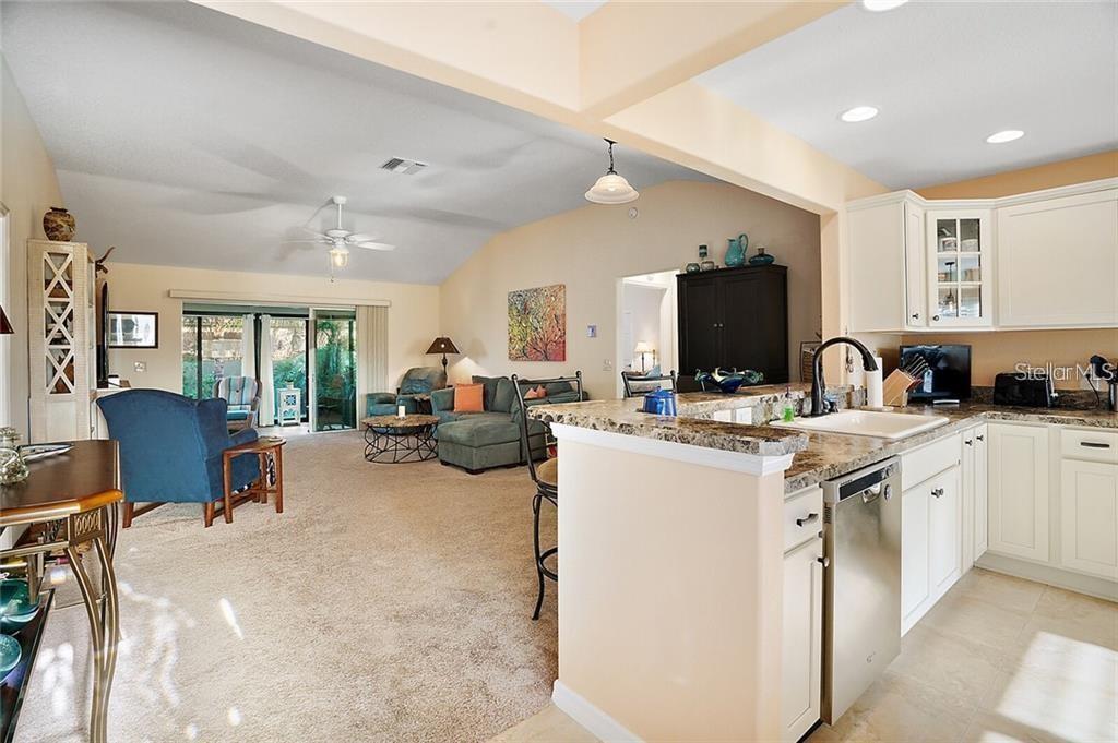 A kitchen with granite countertops and white cabinets opens into a carpeted living room area — 3225 WISE WAY, THE VILLAGES, FL