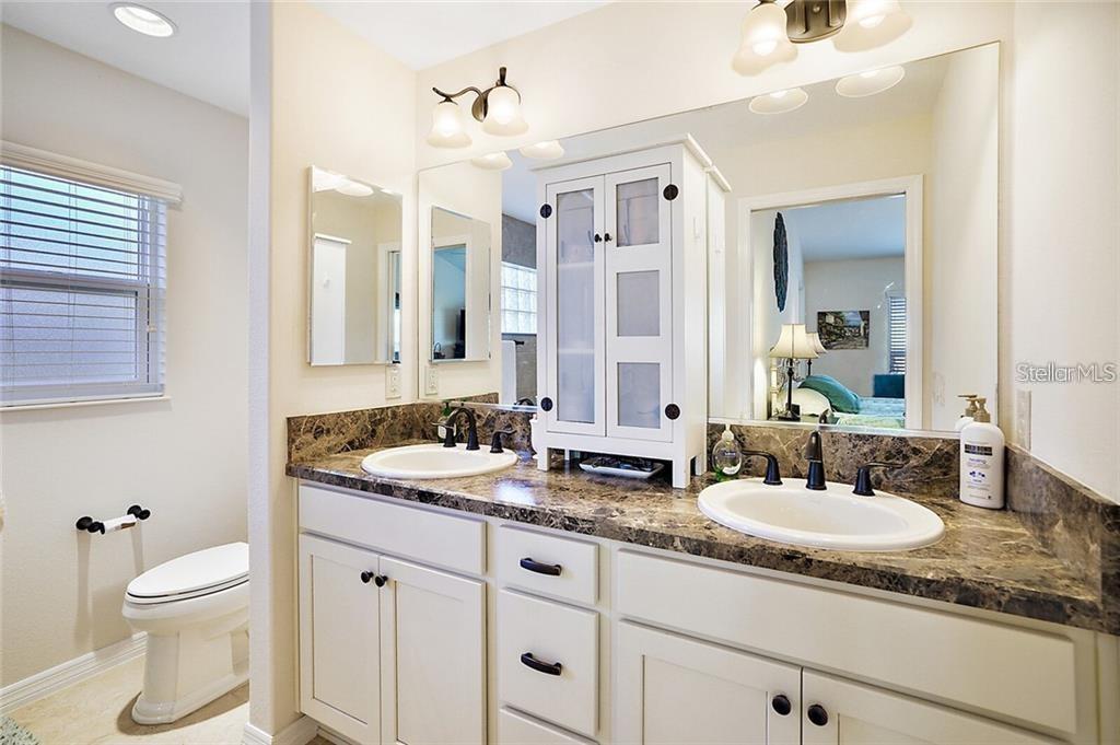 A bathroom features a double vanity with a marble countertop, white cabinets, and two sinks — 3225 WISE WAY, THE VILLAGES, FL