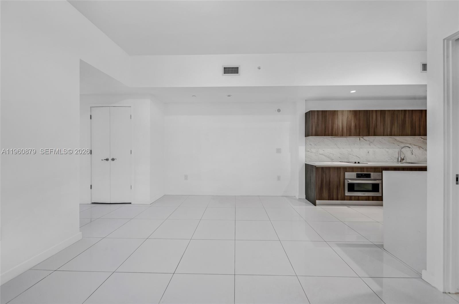 An open-plan room features white tile flooring, a white wall, and a modern kitchen — 851 NE 1st Ave # 204, Miami FL 33132, MIAMI, FL