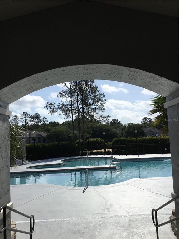 A view through an arched entryway looking out onto a swimming pool and surrounding trees — 3705 SW 27TH STREET UNIT 422, GAINESVILLE, FL