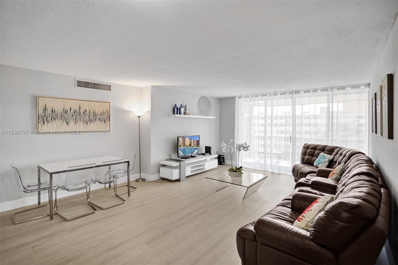 A living room features light wood flooring, a brown leather sectional, and a dining area — 1770 NE 191st St # 1, Miami FL 33179, MIAMI, FL