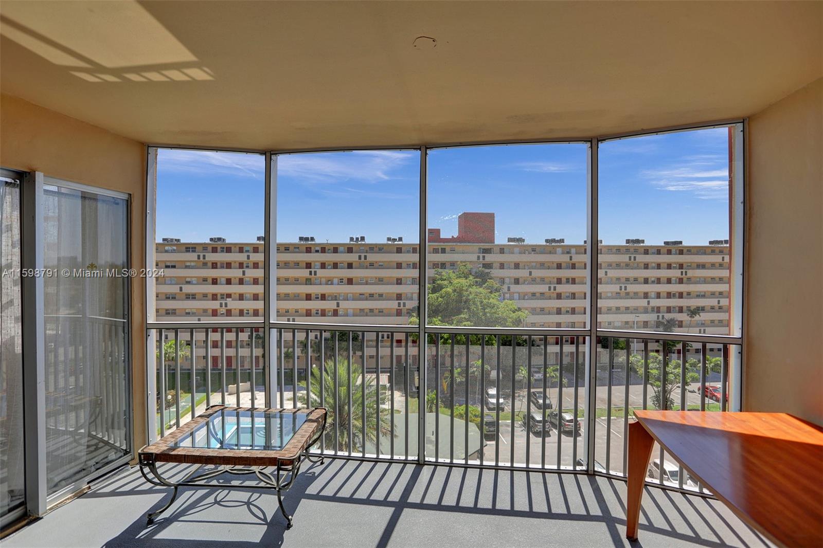A screened-in balcony features a glass-topped table, a wooden desk, and views of a parking lot — 1770 NE 191st St # 1, Miami FL 33179, MIAMI, FL