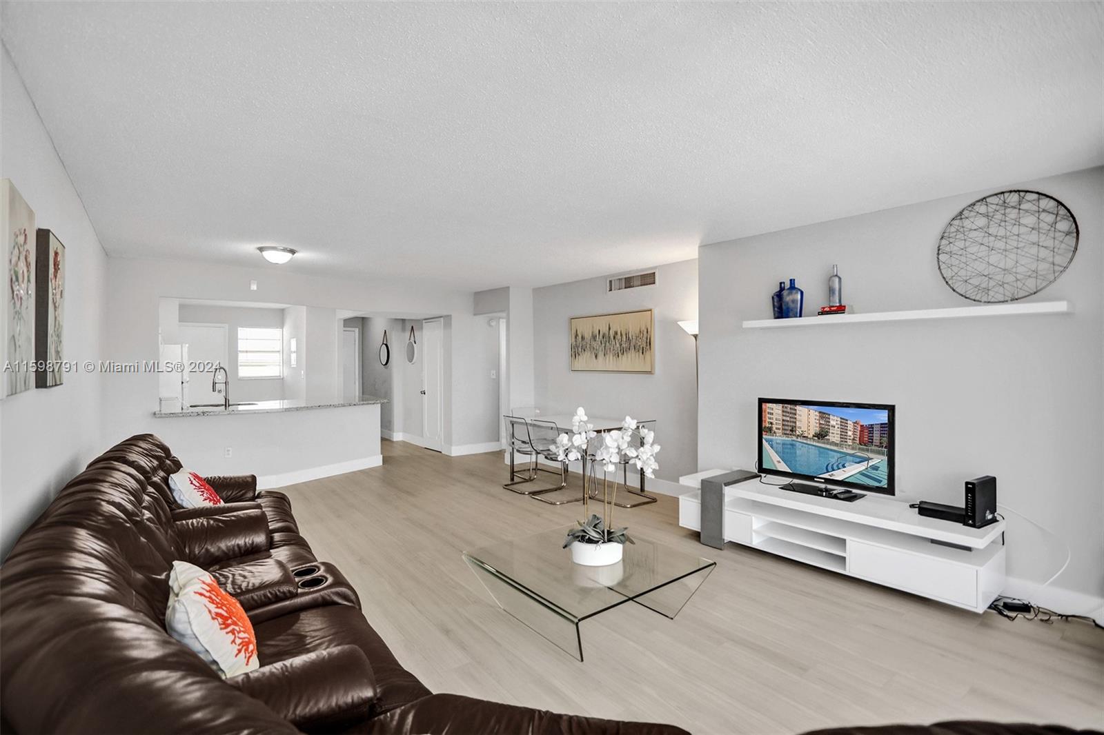 A living room features a brown leather sofa, a glass coffee table, and a white media console — 1770 NE 191st St # 1, Miami FL 33179, MIAMI, FL