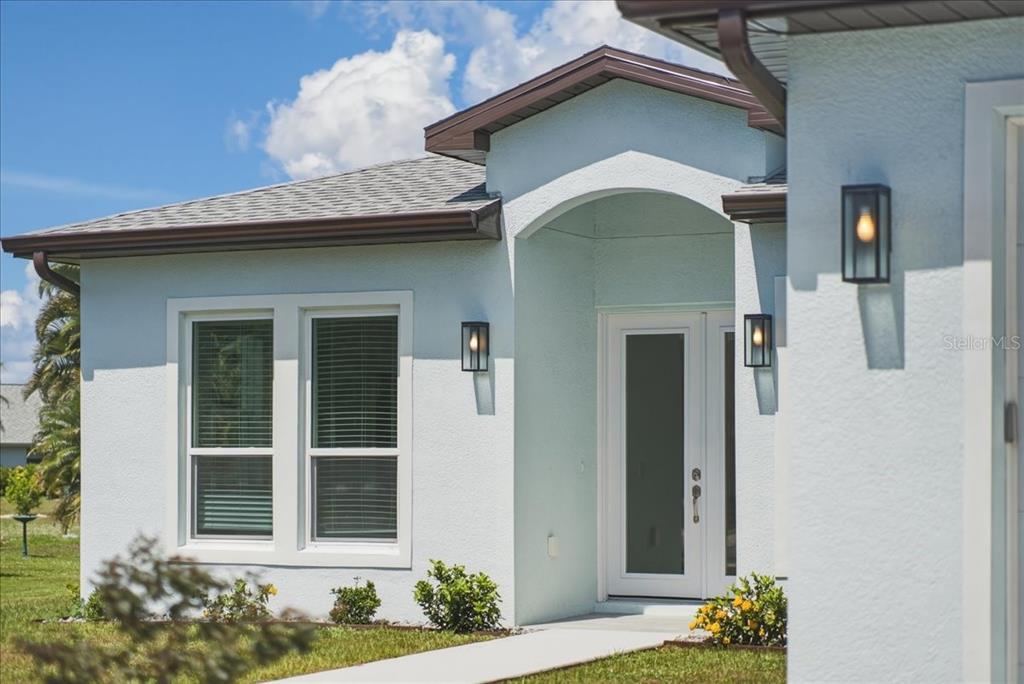 A light blue house exterior features a covered entryway, white-framed windows, and modern wall lanterns — 1215 RIO DE JANEIRO AVENUE, PUNTA GORDA, FL