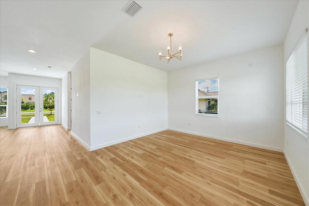 An empty room with light wood flooring, white walls, a chandelier, and glass double doors — 1215 RIO DE JANEIRO AVENUE, PUNTA GORDA, FL