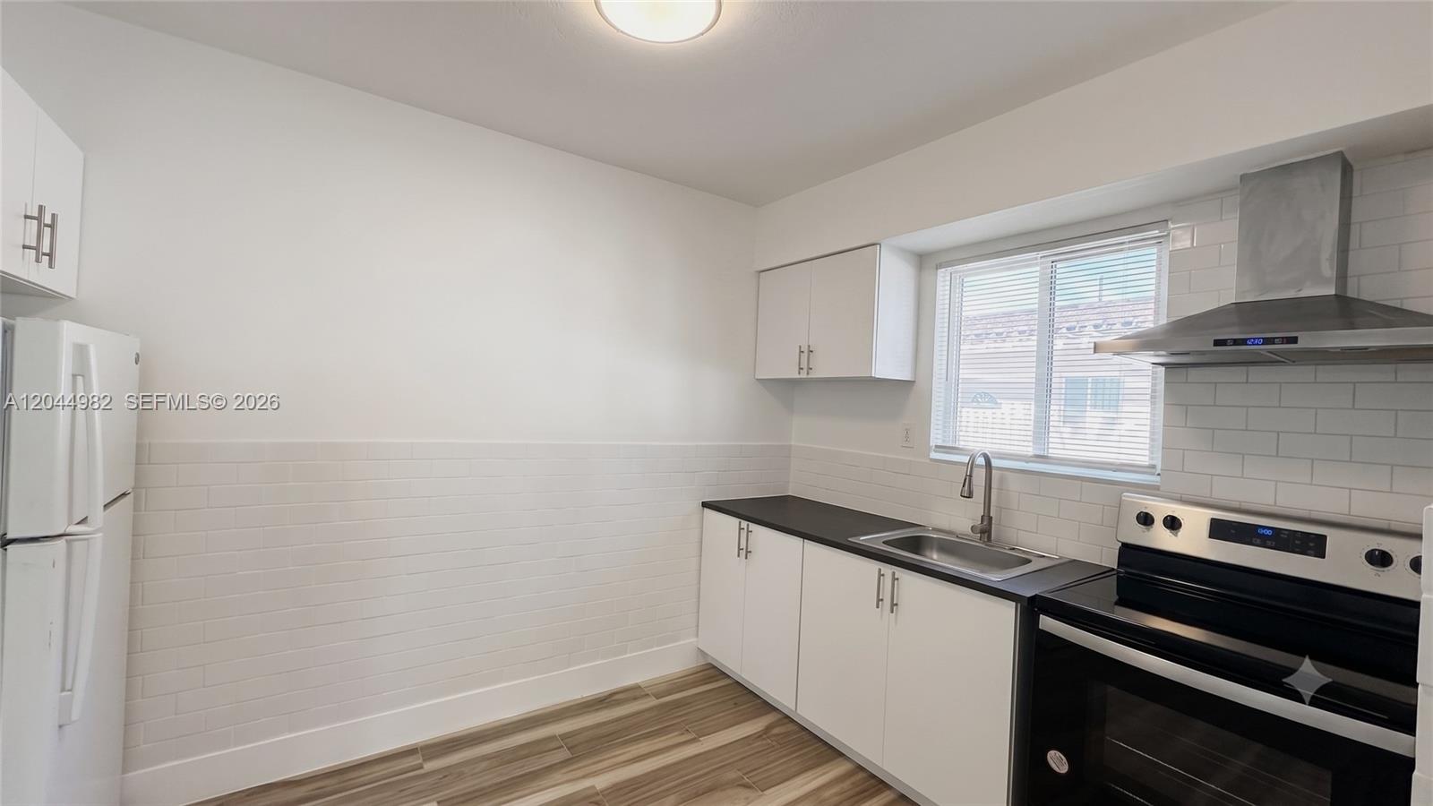 A kitchen features white cabinets, black countertops, a subway tile backsplash, and stainless steel appliances — 120 NE 55th St # 4, Miami FL 33137, MIAMI, FL