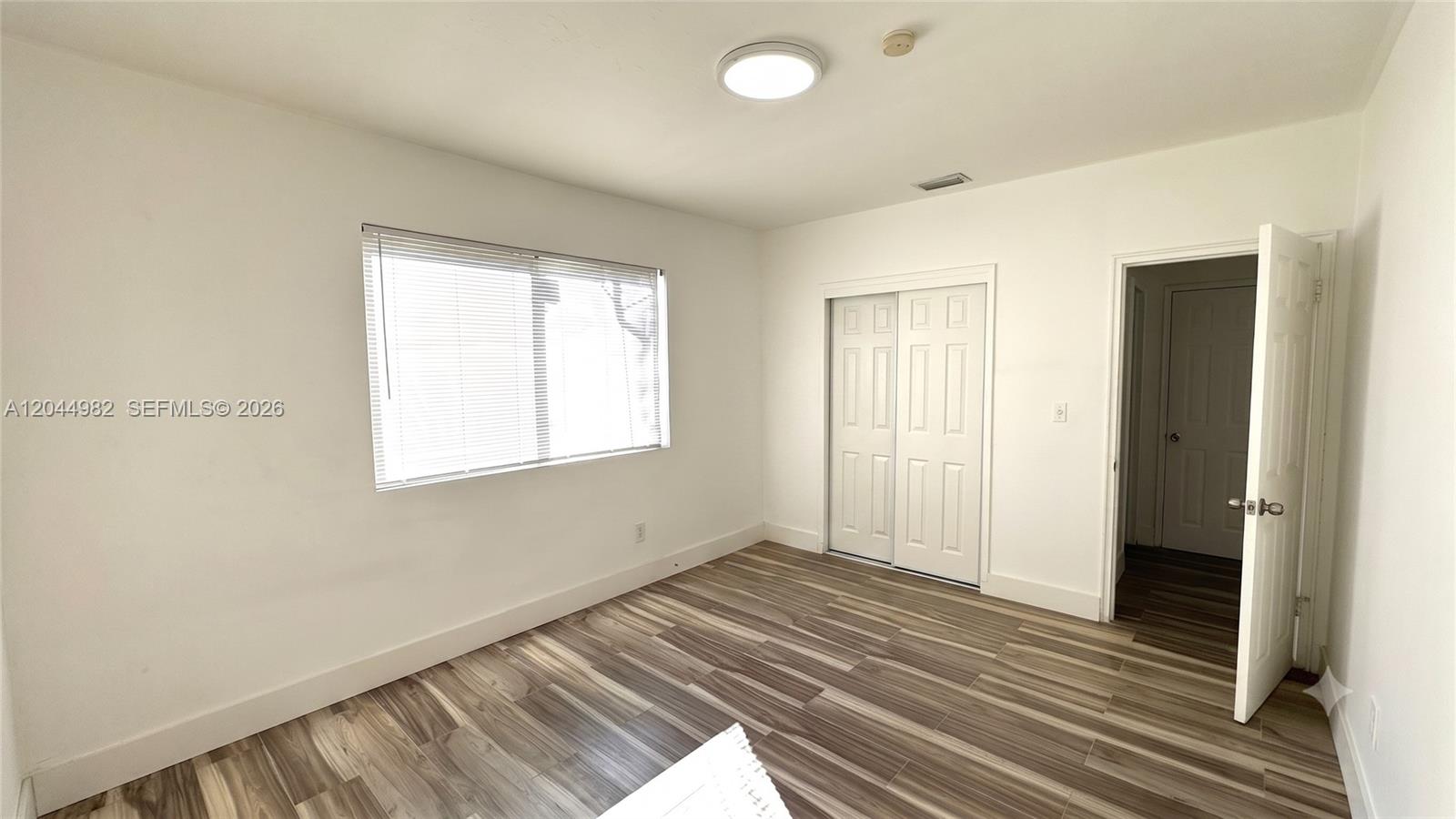 An empty bedroom features white walls, wood-look flooring, a window with blinds, and closet doors — 120 NE 55th St # 4, Miami FL 33137, MIAMI, FL