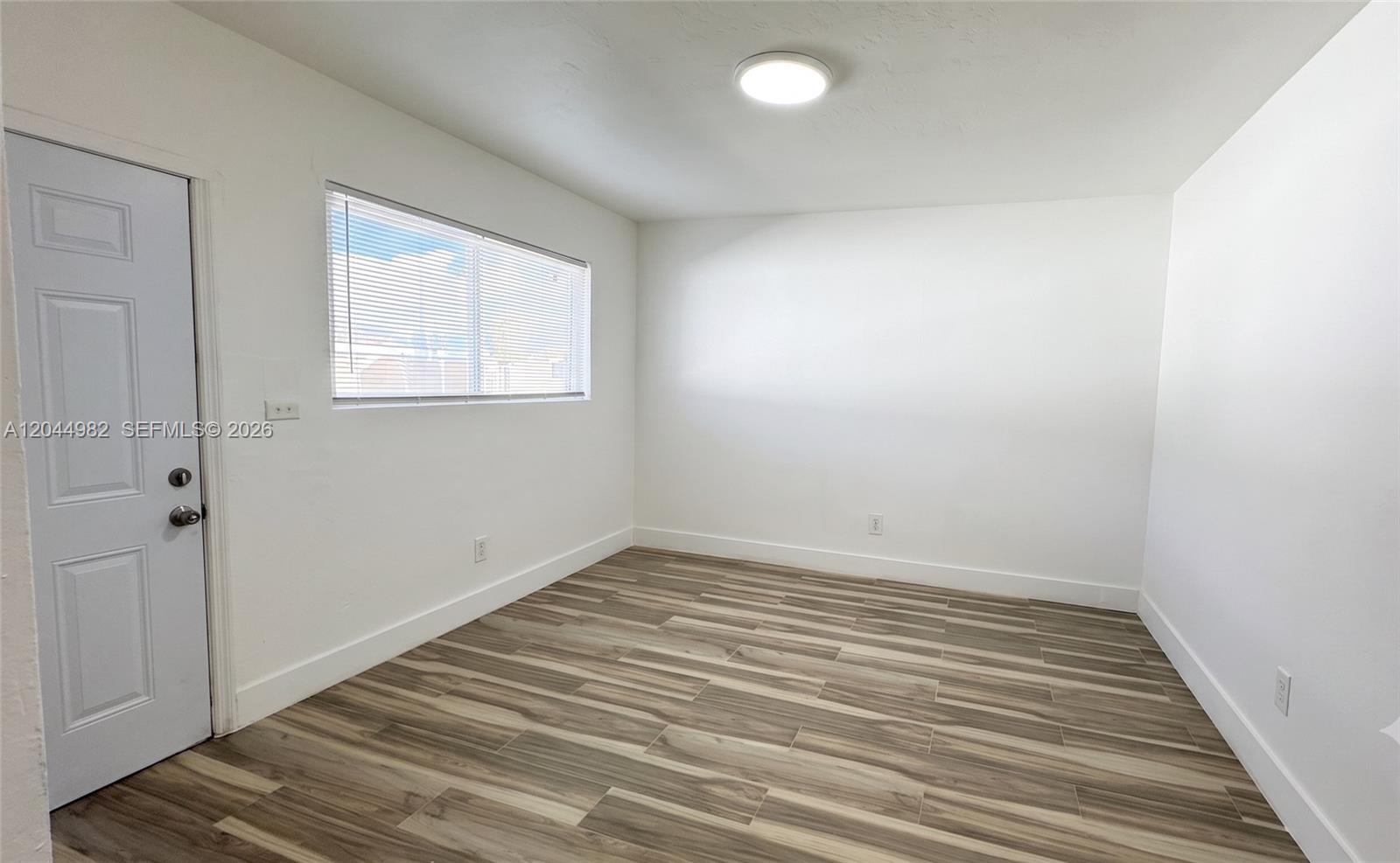 An empty room features white walls, a single window with blinds, and wood-look flooring — 120 NE 55th St # 4, Miami FL 33137, MIAMI, FL
