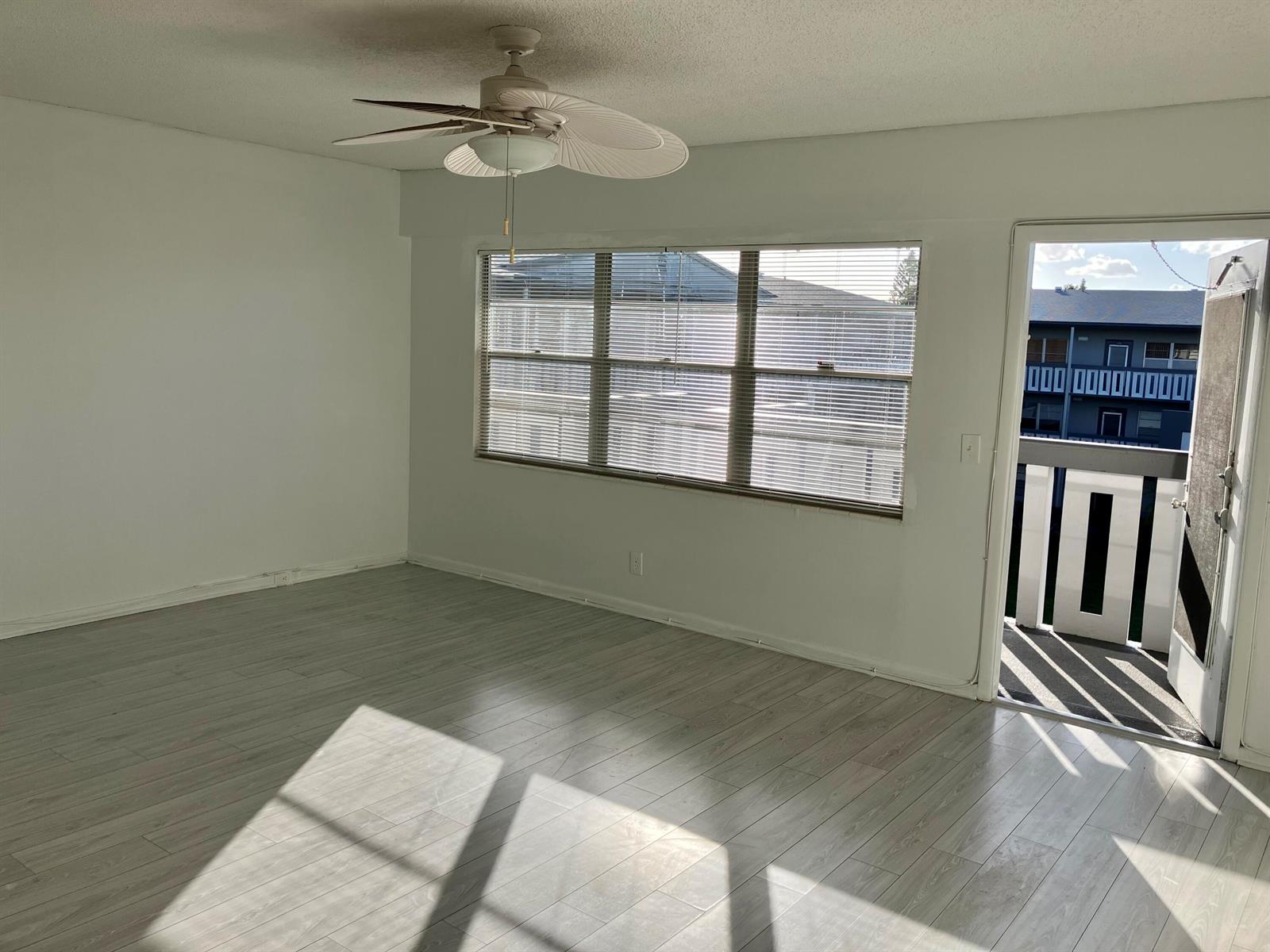 An empty room with light wood-look flooring, a ceiling fan, large windows, and a balcony — 156 Suffolk D, Boca Raton FL 33434, BOCA RATON, FL