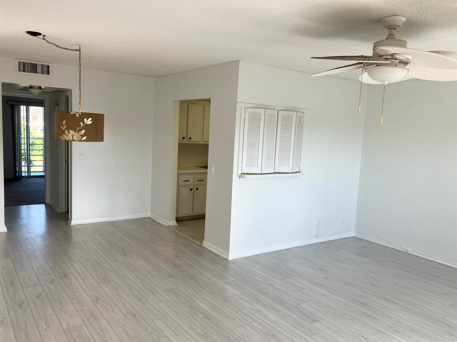 An open living area features light wood-look flooring, a ceiling fan, and a pass-through window — 156 Suffolk D, Boca Raton FL 33434, BOCA RATON, FL