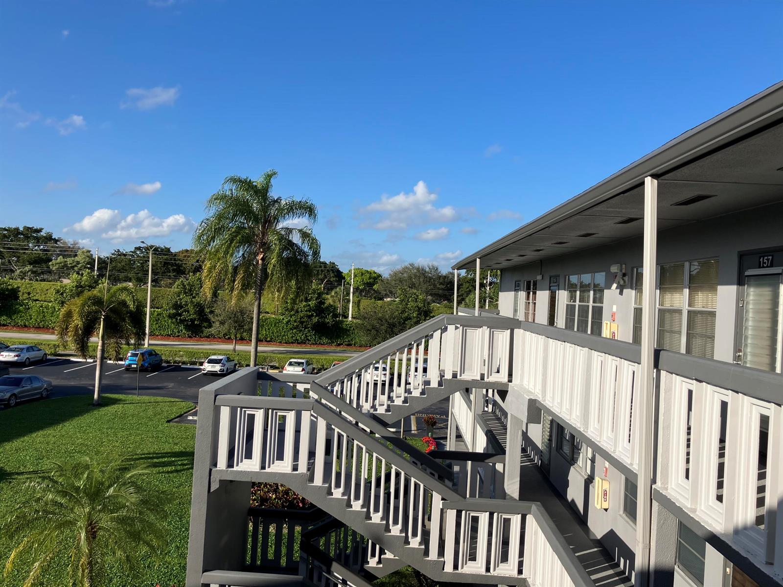 An exterior view of a multi-story apartment building with a concrete staircase and palm trees — 156 Suffolk D, Boca Raton FL 33434, BOCA RATON, FL