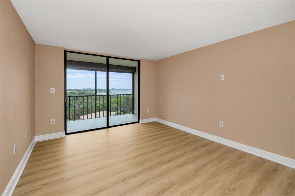 An empty room with light wood-look flooring, tan walls, and a sliding glass door to a balcony — 1324 PASADENA AVENUE S UNIT 605, ST PETERSBURG, FL