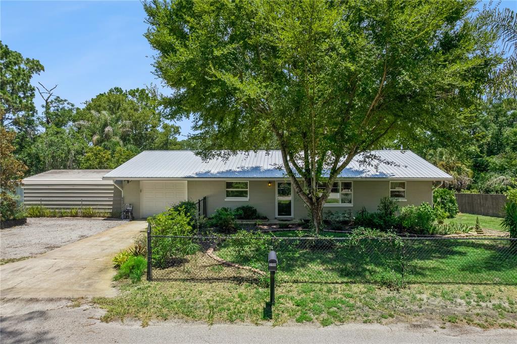A single-story house with a metal roof, attached carport, and a chain-link fenced front yard — 37400 SAINT LOUIS AVENUE, UMATILLA, FL