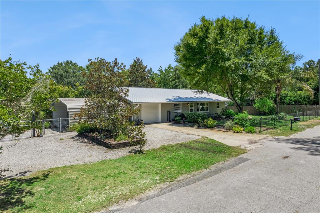 A single-story house with a metal roof, gravel driveway, and attached carport — 37400 SAINT LOUIS AVENUE, UMATILLA, FL